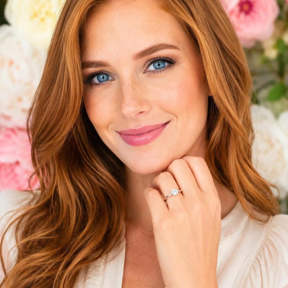 Woman wearing a sterling silver round-cut 4-prong moissanite engagement ring. Model image for size and styling reference — not a photo of the actual ring.