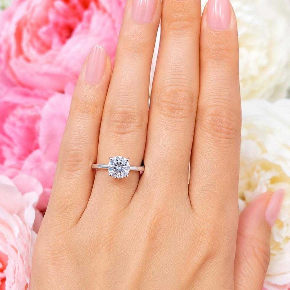 Woman's hand wearing a sterling silver 8.5mm round-cut 4-prong moissanite engagement ring. Model image for size and styling reference — not a photo of the actual ring.