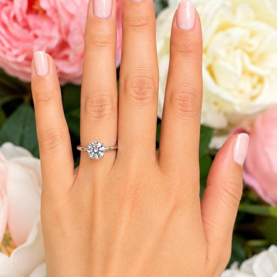Woman's hand wearing a sterling silver 8mm round-cut 4-prong moissanite engagement ring. Model image for size and styling reference — not a photo of the actual ring.