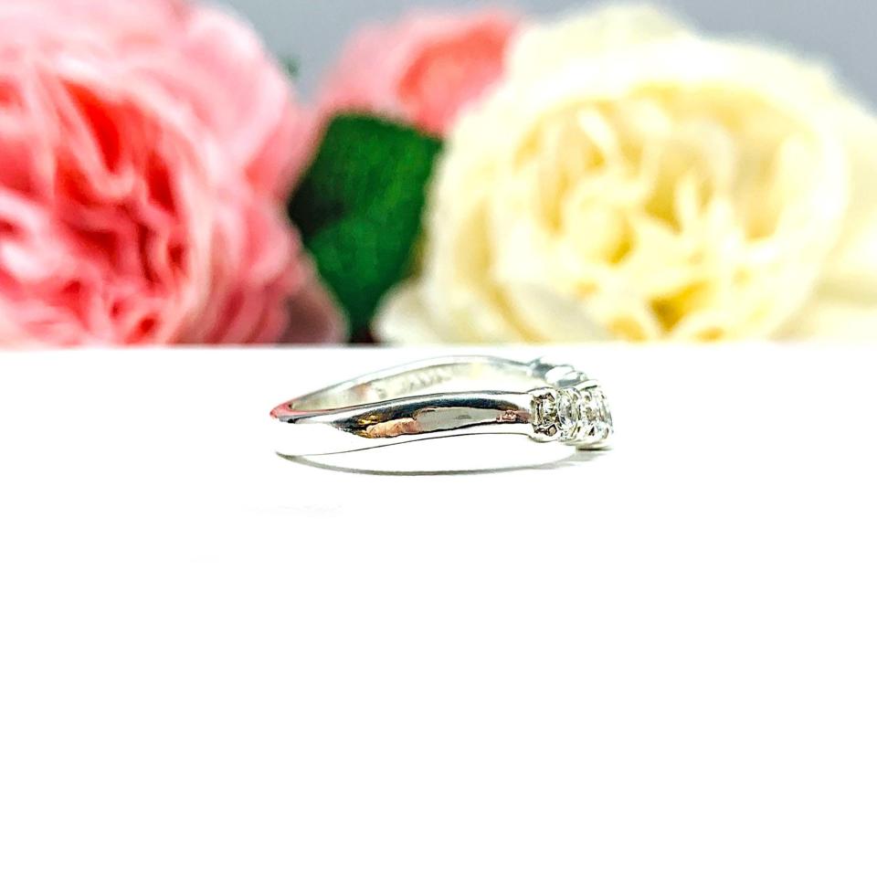 Sterling silver 5-stone curved wedding band featuring 3mm round precision faceted near colorless cubic zirconia stones in prong settings, displayed against a soft floral background.