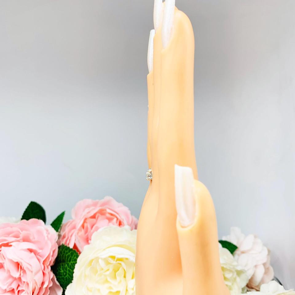Mannequin hand with long white shimmery nails, displayed against a soft white-gray background with pink and white floral accents. The hand is wearing a sterling silver 5-stone curved wedding band featuring 3mm round precision faceted near colorless cz stones in prong settings.