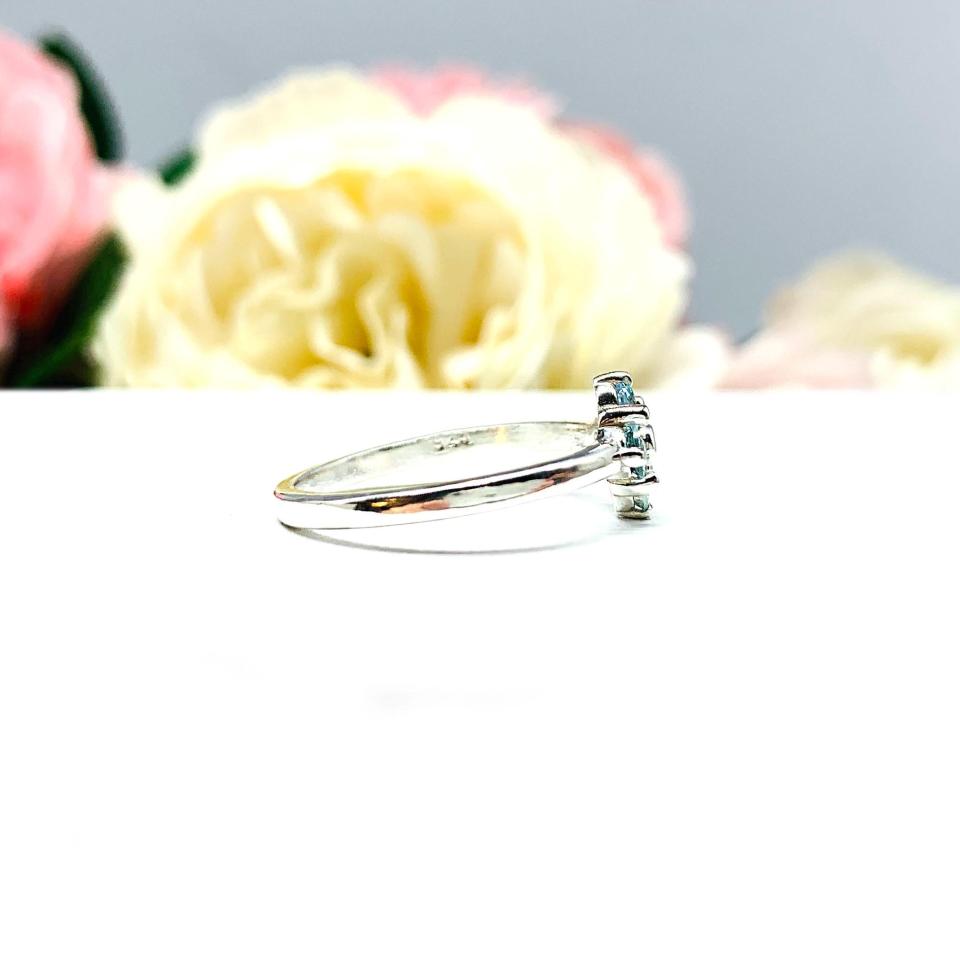 Sterling silver cluster ring featuring four 3mm round light blue aquamarine gemstones. Displayed against a soft-focus floral background, the ring sparkles with contrast and elegance.