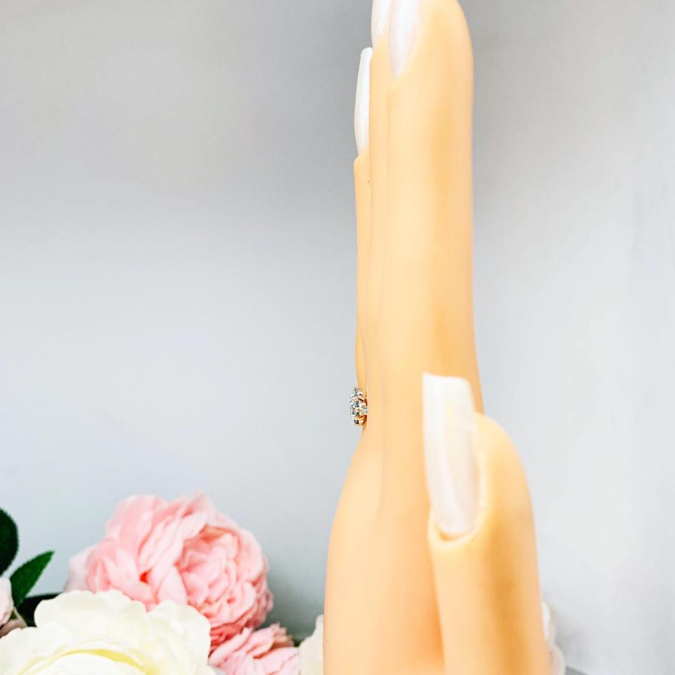 Mannequin hand with long white shimmery nails, displayed against a soft white-gray background with pink and white floral accents. The hand is wearing a sterling silver  cluster ring featuring four 3mm round light blue aquamarine gemstones.