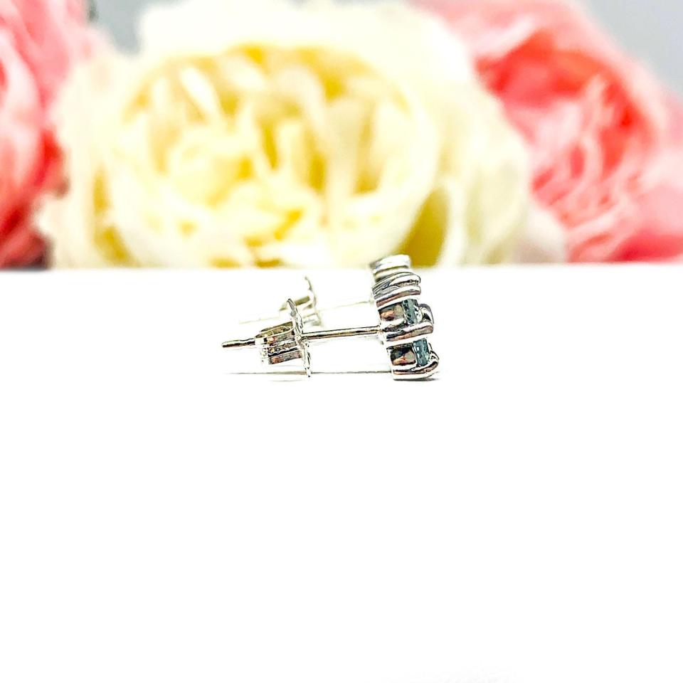 Sterling silver cluster earrings featuring four 3mm round light blue aquamarine gemstones. Displayed against a soft-focus floral background, the earrings sparkle with contrast and elegance.
