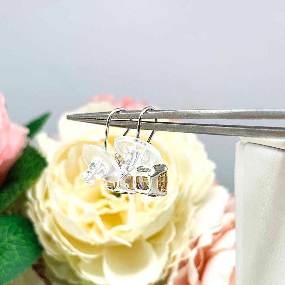 A pair of sterling silver 4-prong dangle earrings with cushion cut champagne cubic zirconia stones. Each dangle is suspended from a thin earwire that comes with a silicone back.