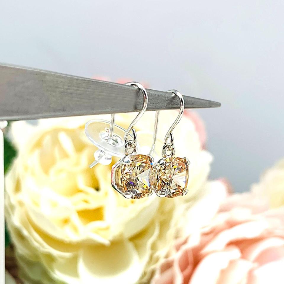 A pair of sterling silver 4-prong dangle earrings with cushion cut champagne cubic zirconia stones. Each dangle is suspended from a thin earwire that comes with a silicone back.