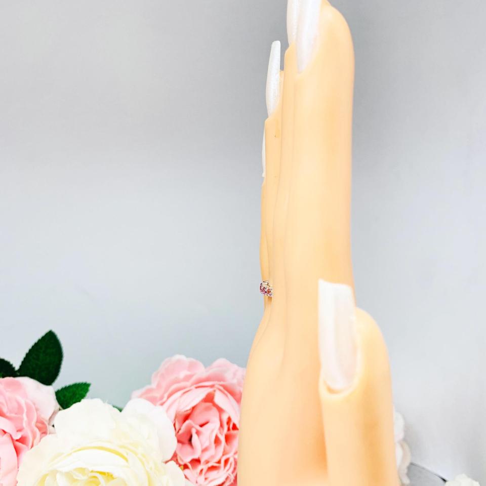 Mannequin hand with long white shimmery nails, displayed against a soft white-gray background with pink and white floral accents. The hand is wearing a sterling silver  twelve stone band set with 2.5mm round gemstones in this configuration: four white topaz, four pink tourmaline and four light pink tourmaline set in a shared prong setting.