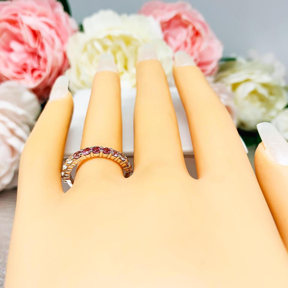 Mannequin hand with long white shimmery nails, displayed against a soft white-gray background with pink and white floral accents. The hand is wearing a sterling silver  twelve stone band set with 2.5mm round gemstones in this configuration: four white topaz, four pink tourmaline and four light pink tourmaline set in a shared prong setting.