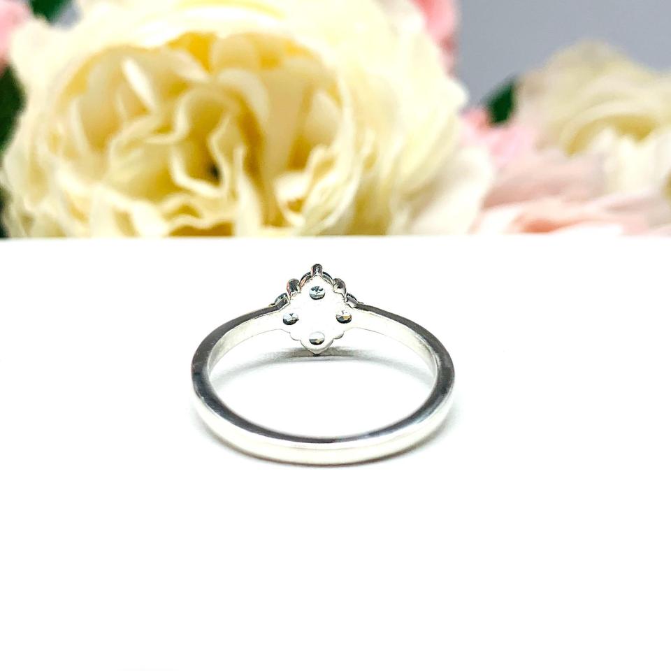 Sterling silver cluster ring featuring four 3mm round light blue aquamarine gemstones. Displayed against a soft-focus floral background, the ring sparkles with contrast and elegance.