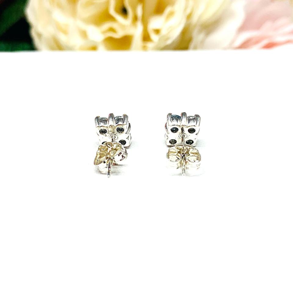 Sterling silver cluster earrings featuring four 3mm round light blue aquamarine gemstones. Displayed against a soft-focus floral background, the earrings sparkle with contrast and elegance.
