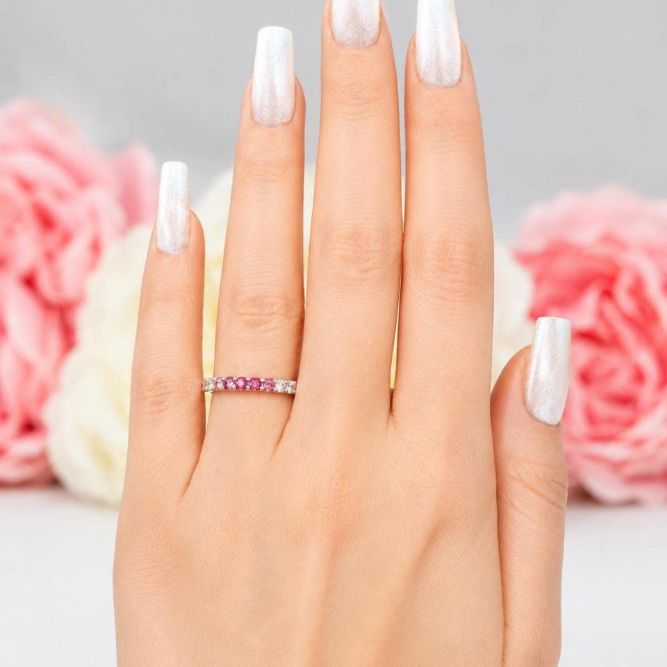 A woman's hand wearing a sterling silver twelve stone band set with 2.5mm round gemstones in this configuration: four white topaz, four pink tourmaline and four light pink tourmaline set in a shared prong setting. Model image for size and styling reference — not a photo of the actual necklace.