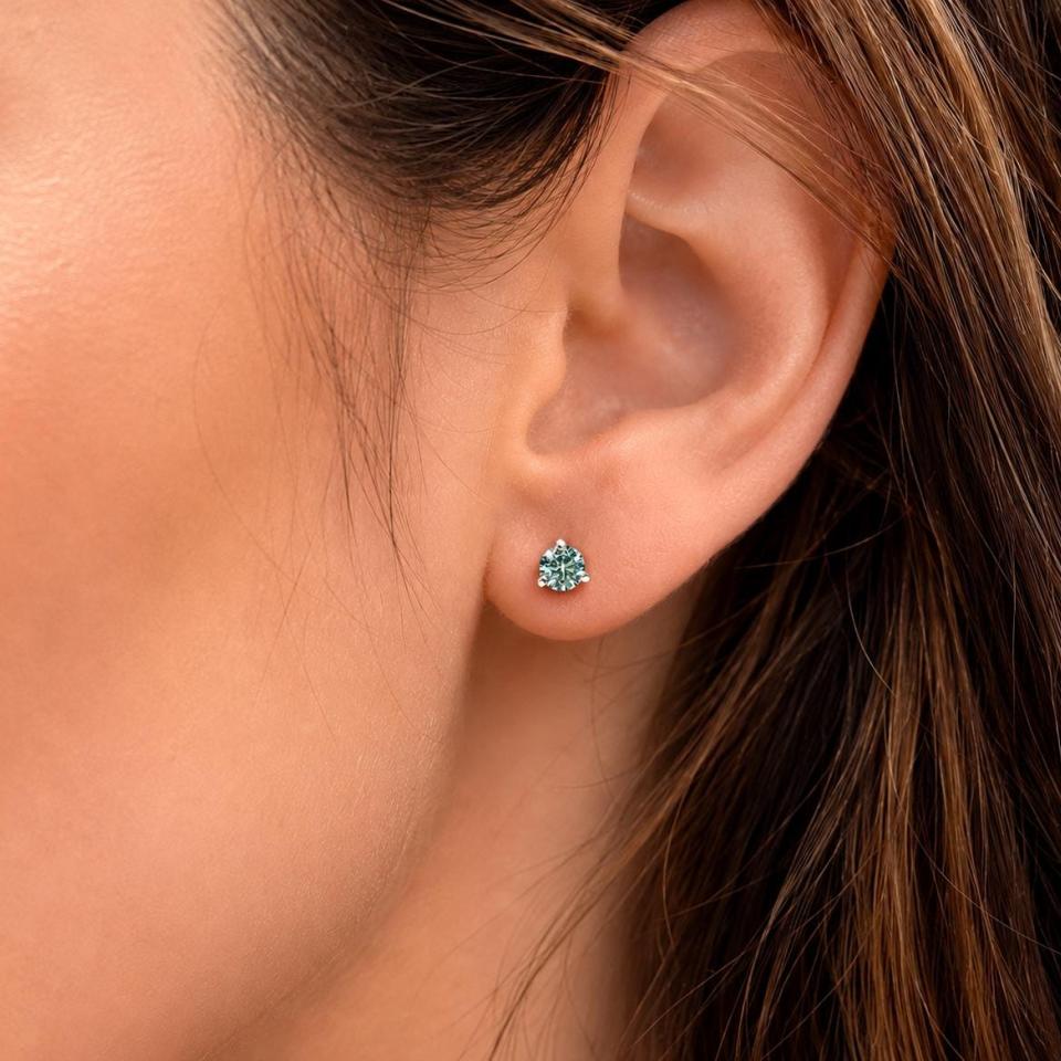 Woman wearing 5mm round sea foam green moissanite martini stud earrings. Model image for size and styling reference — not a photo of the actual earrings.