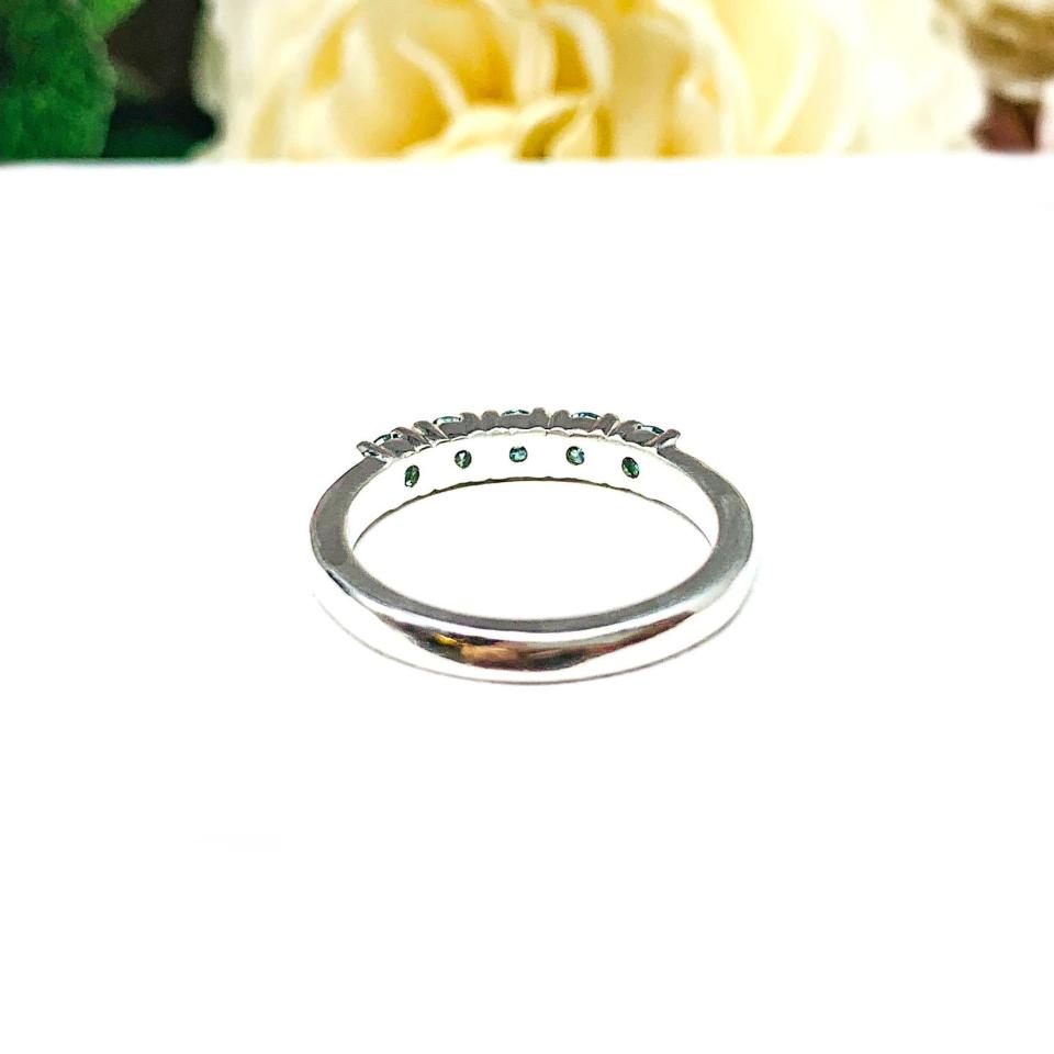 A sterling silver 5-stone band set with 3mm round sparkling aquamarine blue moissanites. Displayed on a white surface with a floral background.