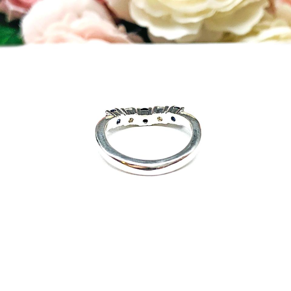 A sterling silver curved 5-stone band featuring alternating round lab blue sapphires and moissanites. The band has a classic design with the gemstones set in a row with three sapphires and two moissanites. Displayed on a white surface with a pastel floral background.