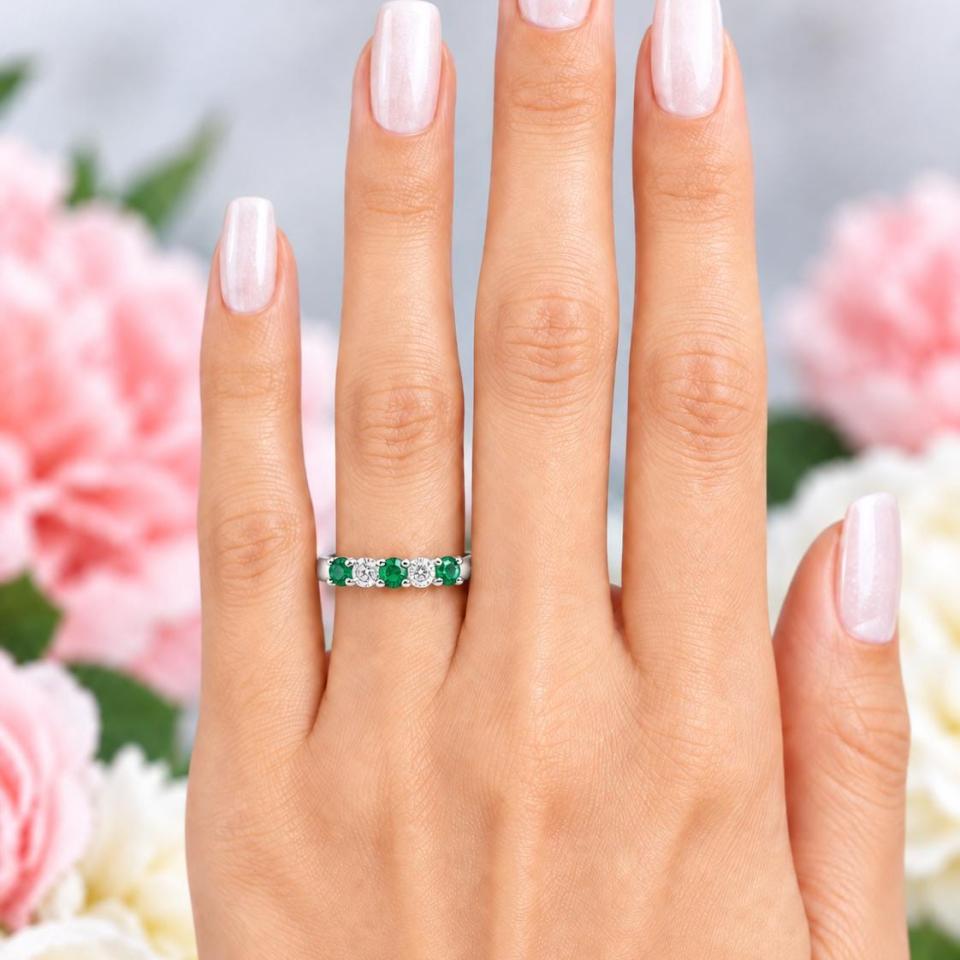 A woman's hand wearing a sterling silver five-stone wedding band with three 3mm round lab-created emeralds and two 3mm round DEF moissanites. Model image for size and styling reference — not a photo of the actual ring.