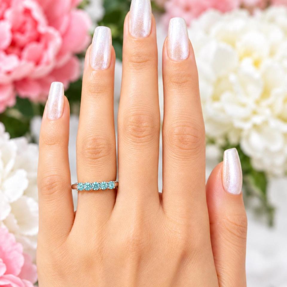 A woman's hands wearing a sterling silver 5-stone band set with 3mm round sparkling aquamarine blue moissanites. Model image for size and styling reference — not a photo of the actual ring.