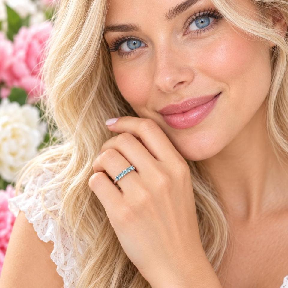 A woman wearing a sterling silver 5-stone band set with 3mm round sparkling aquamarine blue moissanites. Model image for size and styling reference — not a photo of the actual ring.