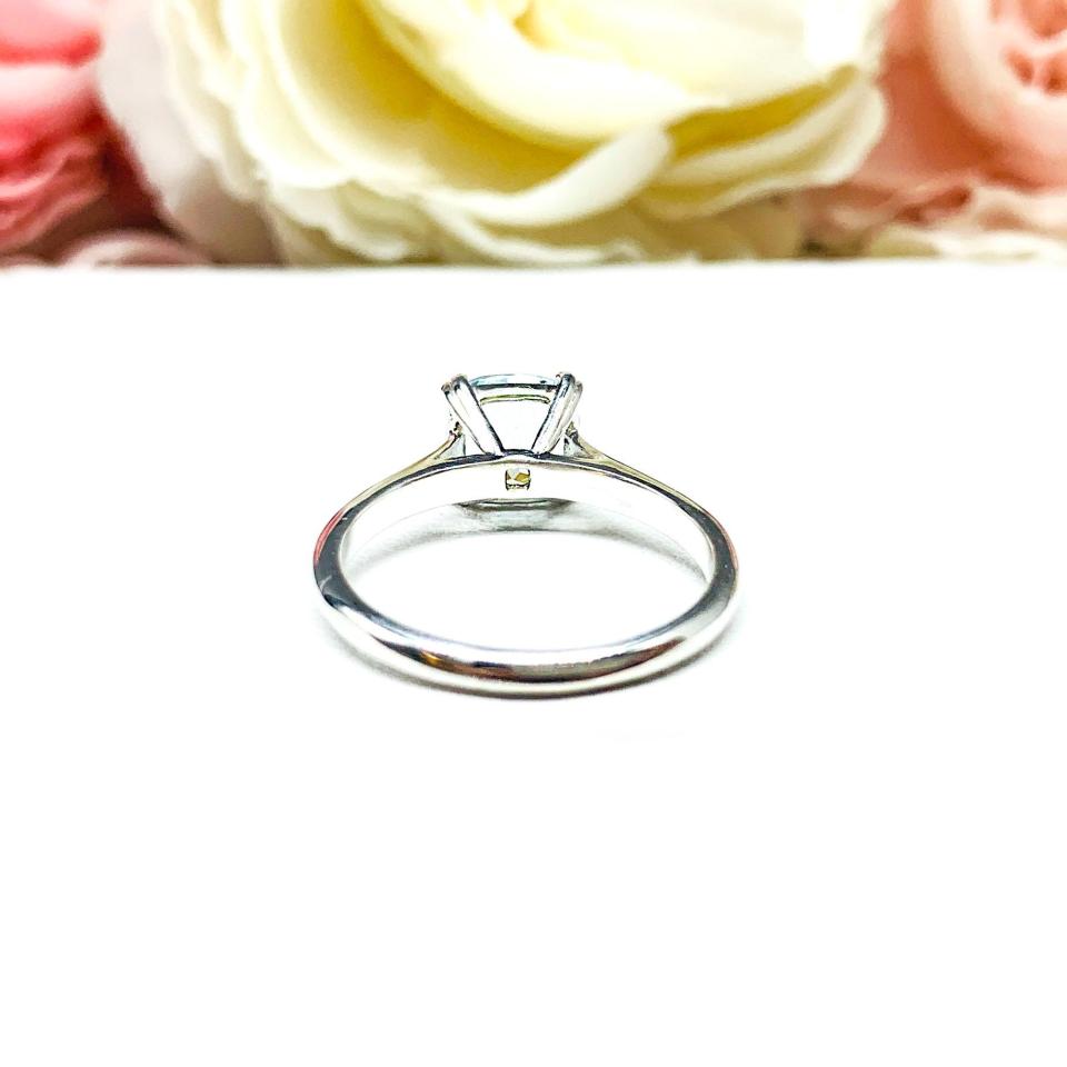 Sterling silver split-prong ring featuring a 7mm cushion-cut light blue aquamarine gemstone. Displayed against a soft-focus floral background, the ring sparkles with contrast and elegance.