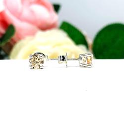 A pair of silver stud earrings set with round brilliant cut light champagne cubic zirconias.  The four prong basket earrings are on a white surface with the left earring facing forward and the right earring facing to the right to showcase the brilliant cutting of the czs, center post and butterfly friction clasp.