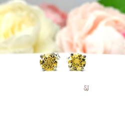 A pair of silver stud earrings set with 6mm round natural golden citrine gemstones. The four prong basket earrings are on a white surface with both earrings facing front to showcase the crisp clarity and golden yellow color of the stones.