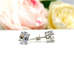 A pair of silver basket stud earrings set with oval brilliant cut cubic zirconias.  The four prong earrings are on a white surface with the left earring facing forward to showcase the clear clarity and excellent faceting of the czs and the right earring facing to the right to display the basket setting, center post and butterfly friction clasp.