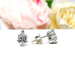 Pair of pear-shaped CZ stud earrings in sterling silver 6-prong settings, displayed with soft floral accents.