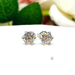 A pair of silver stud earrings set with round brilliant cut 'near colorless or 'G color'  cubic zirconias.  The 6 prong earrings are on a white surface with both earrings facing front to showcase the brilliant cutting of the czs. The text 'SJ' appears in pink to the right, below the earrings.