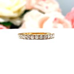 A 10k rose gold 2mm round moissanite wedding band resting on a white surface with pink and white flowers in the background.