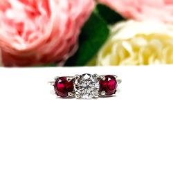 A sterling silver 3-stone ring with a 6mm round brilliant cut cubic zirconia center that radiates icy sparkle, flanked by two 5mm round deep red lab-created rubies.