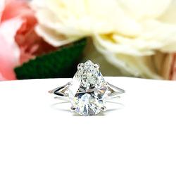 An elegant sterling silver engagement ring featuring a 13x9mm near colorless precision-cut pear cubic zirconia. Displayed on a white surface with a floral background.