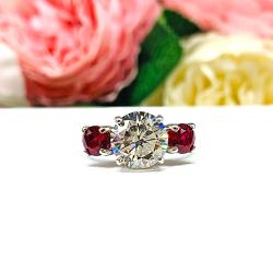 A sterling silver 3-stone ring with a 9mm near colorless round brilliant cut cubic zirconia center that radiates icy sparkle, flanked by two 5mm round deep red lab-created rubies.