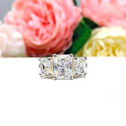 Sterling silver 3-stone engagement ring featuring a 9x7mm radiant cut cubic zirconia center stone with two 7x5mm radiant CZ side stones. The highly polished wide band tapers for comfort. Displayed on a white surface with soft floral background.