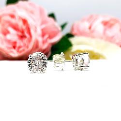 A pair of sterling silver basket stud earrings set with round mixed-brilliant cut lab white sapphires shown on a white surface with pink and white flowers in the background.