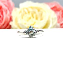 Sterling silver cluster ring featuring four 3mm round light blue aquamarine gemstones. Displayed against a soft-focus floral background, the ring sparkles with contrast and elegance.