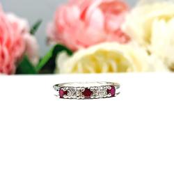 A sterling silver 5-stone band featuring alternating round lab rubies and moissanites. The band has a classic design with the gemstones set in a row with three rubies and two moissanites. Displayed on a white surface with a pastel floral background.