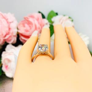 Mannequin hand with long white shimmery nails, displayed against a soft white-gray background with pink and white floral accents. The hand is wearing a near colorless (G/H/I color) round brilliant cut cubic zirconia solitaire ring in a split prong cathedral setting. The ring is made of sterling silver and features a sleek, minimalist design. The setting is simple yet elegant, allowing the center stone to take center stage.
