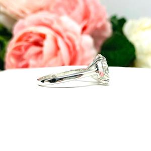 Close-up view of a near colorless (G/H/I color) round brilliant cut cubic zirconia solitaire ring in a split prong cathedral setting. The ring is made of sterling silver and features a sleek, minimalist design. The setting is simple yet elegant, allowing the center stone to take center stage. The ring is displayed against a soft, blurred background of pastel-colored flowers, creating a romantic and delicate ambiance.