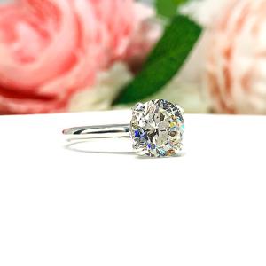 Close-up view of a near colorless (G/H/I color) round brilliant cut cubic zirconia solitaire ring in a split prong cathedral setting. The ring is made of sterling silver and features a sleek, minimalist design. The setting is simple yet elegant, allowing the center stone to take center stage. The ring is displayed against a soft, blurred background of pastel-colored flowers, creating a romantic and delicate ambiance.