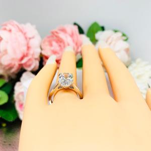 Mannequin hand with long white shimmery nails, displayed against a soft white-gray background with pink and white floral accents. The hand is wearing a sterling silver solitaire engagement ring set with a 12x8mm elongated oval near colorless cubic zirconia. The ring features split prongs and a cathedral shank.