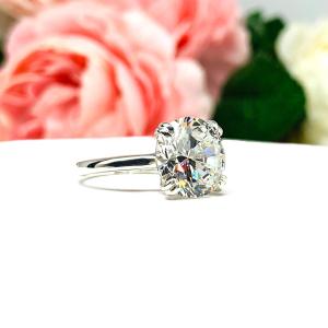 Close-up view of a near colorless (G/H/I color) round brilliant cut cubic zirconia solitaire ring in a split prong cathedral setting. The ring is made of sterling silver and features a sleek, minimalist design. The setting is simple yet elegant, allowing the center stone to take center stage. The ring is displayed against a soft, blurred background of pastel-colored flowers, creating a romantic and delicate ambiance.