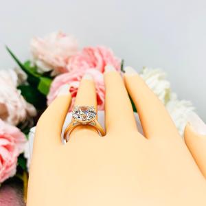 Mannequin hand with long white shimmery nails, displayed against a soft white-gray background with pink and white floral accents. The hand is wearing a near colorless (G/H/I color) round brilliant cut cubic zirconia solitaire ring in a split prong cathedral setting. The ring is made of sterling silver and features a sleek, minimalist design. The setting is simple yet elegant, allowing the center stone to take center stage.