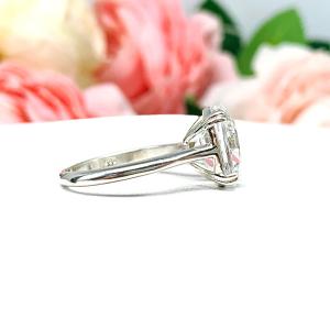 Sterling silver engagement ring featuring a sparkling elongated cushion-cut lab created white sapphire held in a split-prong setting, with soft-focus pink and white flowers in the background.