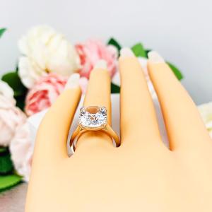 Mannequin hand with long white shimmery nails, displayed against a soft white-gray background with pink and white floral accents. The hand is wearing a sterling silver engagement ring featuring a sparkling elongated cushion-cut lab created white sapphire held in a split-prong setting.
