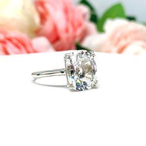 Sterling silver engagement ring featuring a sparkling elongated cushion-cut lab created white sapphire held in a split-prong setting, with soft-focus pink and white flowers in the background.