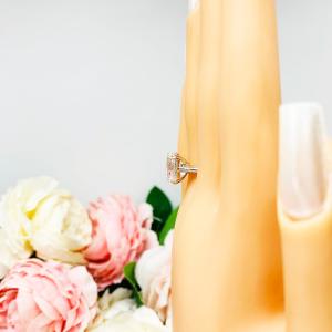 Mannequin hand with long white shimmery nails, displayed against a soft white-gray background with pink and white floral accents. The hand is wearing a sterling silver engagement ring featuring a sparkling elongated cushion-cut lab created white sapphire held in a split-prong setting.