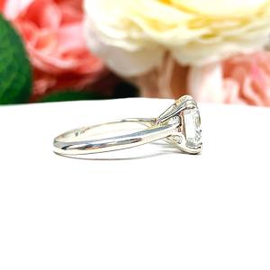Sterling silver 9mm near colorless (G/H color) asscher cut cubic zirconia solitaire engagement ring. The ring is resting on a white surface with a background of pink and white flowers.
