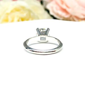 Sterling silver engagement ring set with an 8mm old mine cut near colorless cubic zirconia. The ring is resting on a white surface with a background of soft-focus pink and white flowers.