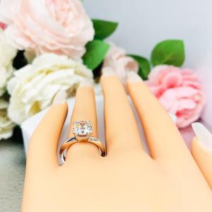 Mannequin hand with long white shimmery nails, displayed against a soft white-gray background with pink and white floral accents. The hand is wearing a sterling silver engagement ring set with an 8mm old mine cut near colorless cubic zirconia.
