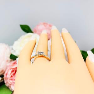 Mannequin hand with long white shimmery nails, displayed against a soft white-gray background with pink and white floral accents. The hand is wearing a dainty 4-prong sterling silver, horizontal east west set engagement ring featuring a precision-faceted marquise cubic zirconia.