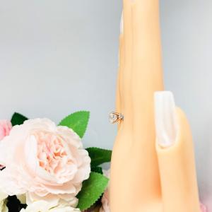 Mannequin hand with long white shimmery nails, displayed against a soft white-gray background with pink and white floral accents. The hand is wearing a sterling silver engagement ring set with an 8mm old mine cut near colorless cubic zirconia.